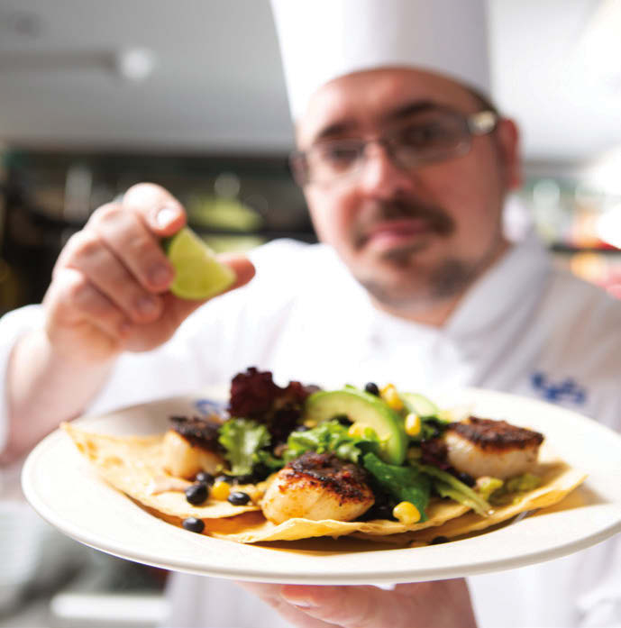 Chef spritzing lemon over a plate.